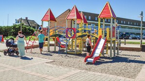 A playground with climbing structures and slides, surrounded by a paved area and a building in the background.