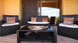 Een terras met wicker meubels, een salontafel met glazen blad en een schuifpui naar een balkon.