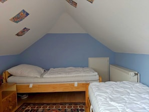 A small, single-bed room with a sloped ceiling, a radiator, and a wooden bed frame.