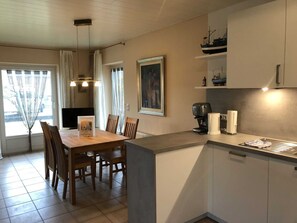 Une cuisine moderne avec un coin repas, comprenant une table et des chaises en bois, une machine à café et une petite maquette de bateau posée sur une étagère.