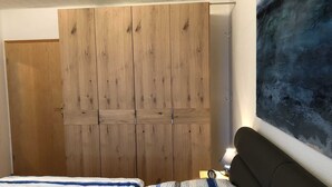 A bedroom with a wooden wardrobe, a bed with striped bedding, and a wall-mounted lamp. - Vacation cottage Seestern, Germany (Friedrichskoog)