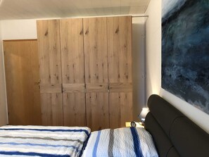 Une chambre avec une armoire en bois, un lit avec une literie à rayures et une lampe fixée au mur.