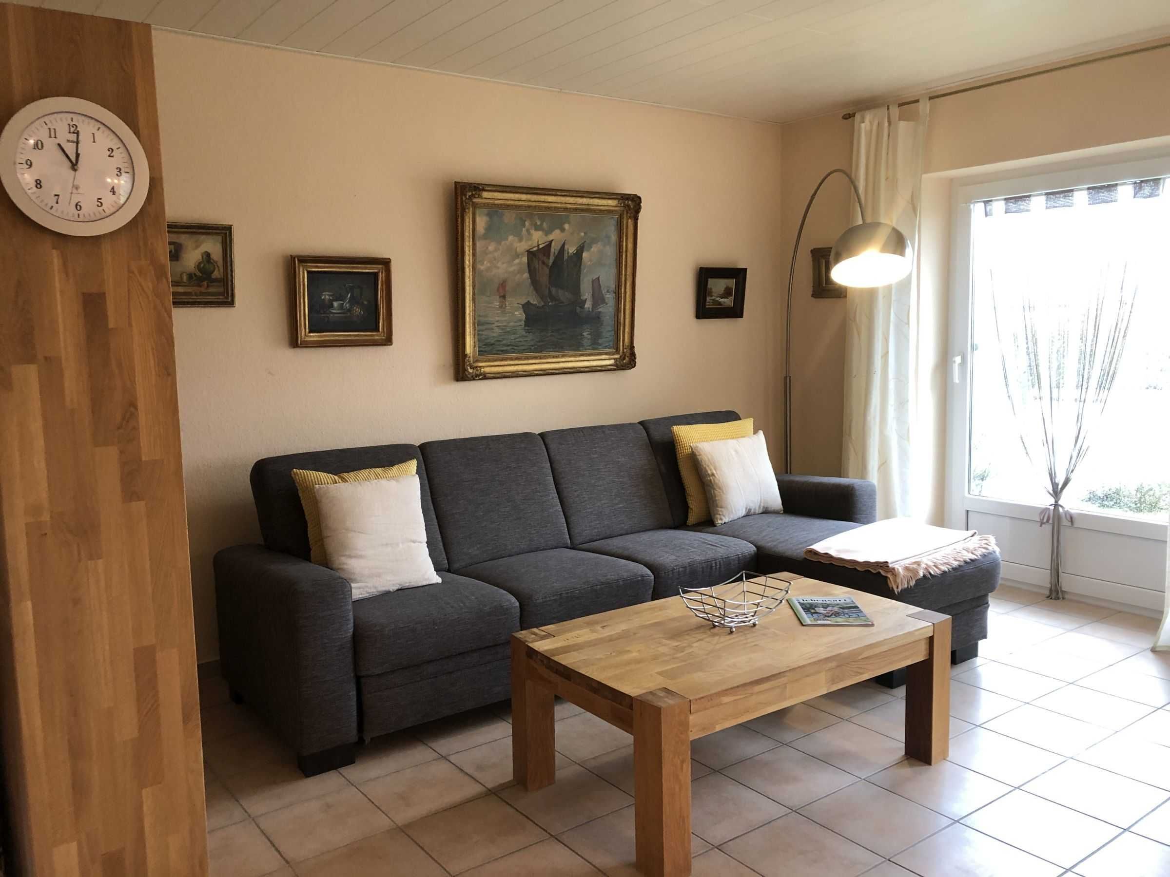 A living room with a dark grey sofa, two white cushions, a wooden coffee table, and a painting of a ship on the wall.