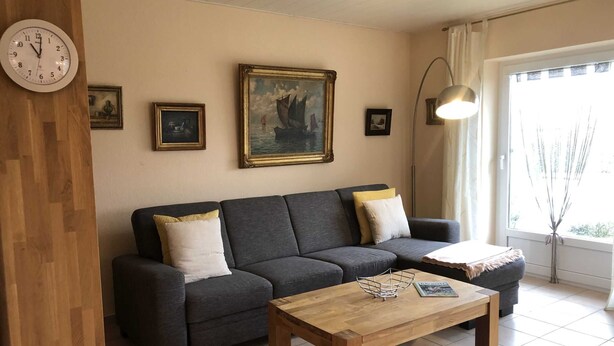 A living room with a dark grey sofa, two white cushions, a wooden coffee table, and a painting of a ship on the wall. - Vacation cottage Seestern, Germany (Friedrichskoog)