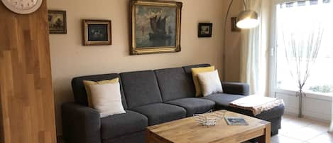 A living room with a dark grey sofa, two white cushions, a wooden coffee table, and a painting of a ship on the wall.
