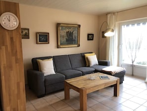 Un salon avec un canapé gris foncé, deux coussins blancs, une table basse en bois et un tableau représentant un navire accroché au mur.
