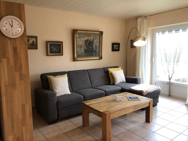 Un salon avec un canapé gris foncé, deux coussins blancs, une table basse en bois et un tableau représentant un navire accroché au mur.