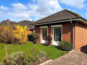 A single-story brick house with a tiled roof, a front door, and a small front yard with grass and shrubs. - Vacation cottage Seestern, Germany (Friedrichskoog)