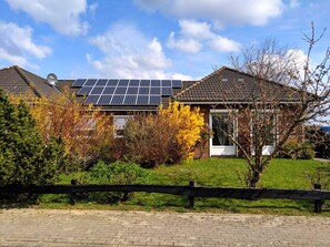 Ein Haus mit Solaranlage auf dem Dach, umgeben von Herbstlaub und einem Ziegelweg.