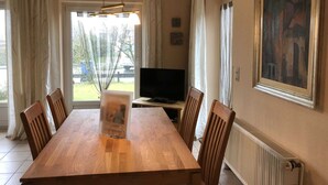 A dining area with a wooden table and chairs, a television, and a painting on the wall. - Vacation cottage Seestern, Germany (Friedrichskoog)