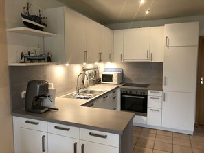 A modern kitchen with white cabinets, a built-in oven, a microwave, and a coffee machine.