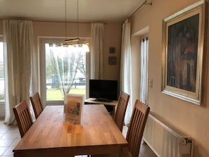 A dining area with a wooden table and chairs, a television, and a painting on the wall. - Vacation cottage Seestern, Germany (Friedrichskoog)