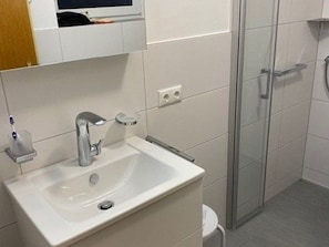 A bathroom with a white sink, a mirror, and a glass shower enclosure. - Vacation cottage Seestern, Germany (Friedrichskoog)