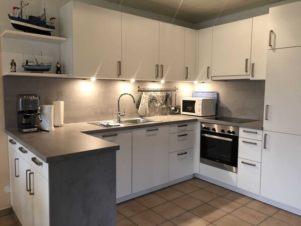 Eine moderne Küche mit weißen Schränken, einer Edelstahl-Spüle, einer Kaffeemaschine, einer Mikrowelle und einem Backofen.