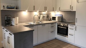A modern kitchen with white cabinets, a stainless steel sink, a coffee maker, a microwave, and an oven. - Vacation cottage Seestern, Germany (Friedrichskoog)