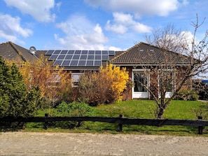 Une maison avec des panneaux solaires sur le toit, entourée d’un feuillage automnal et bordée d’un chemin en briques.