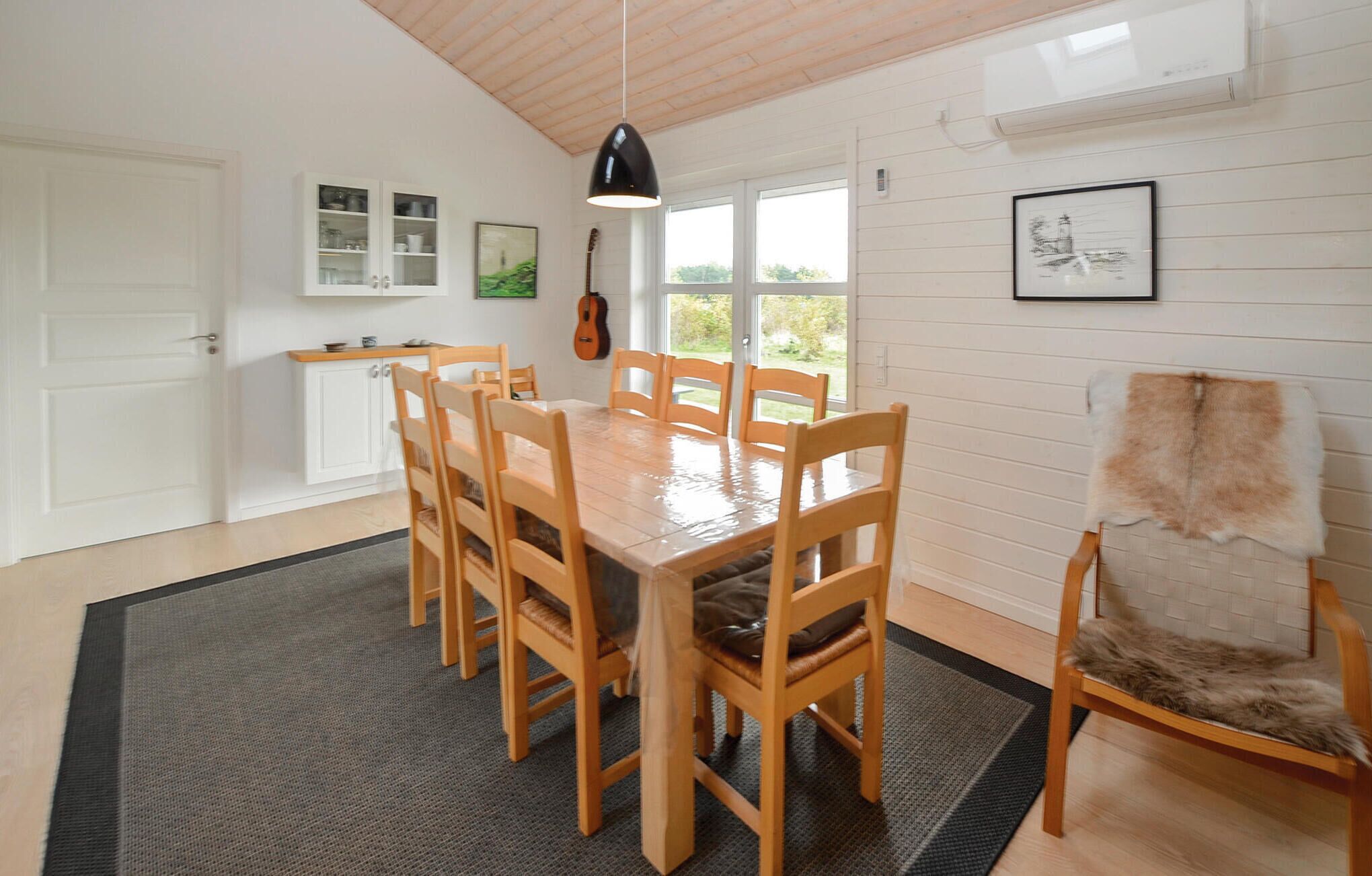 Un coin repas avec une table et des chaises en bois, un luminaire suspendu noir et un fauteuil recouvert de fourrure.