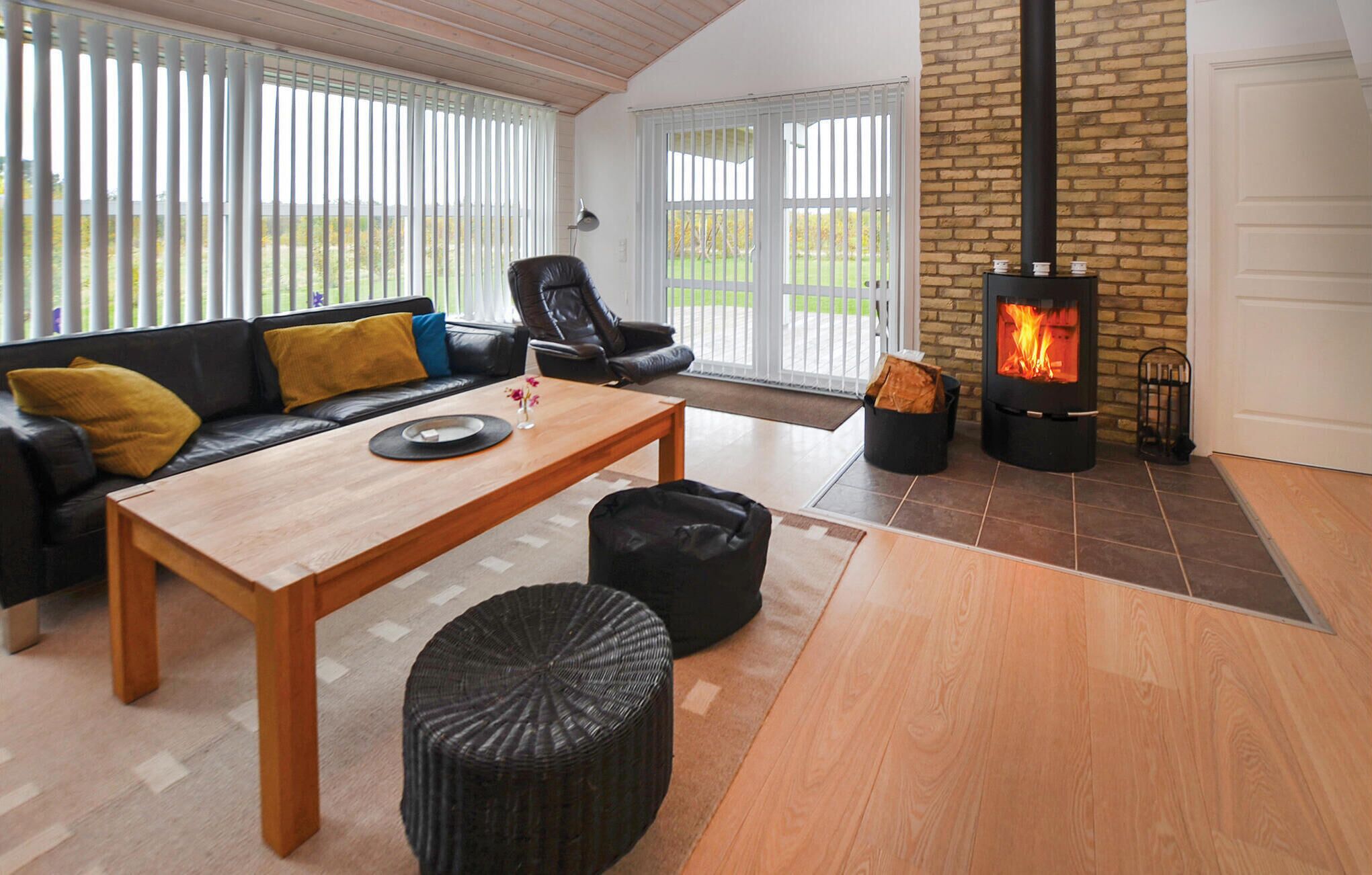 A cozy living room with a sofa, a coffee table, a black pouf, and a wood-burning stove.