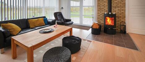A cozy living room with a sofa, a coffee table, a black pouf, and a wood-burning stove.