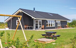 En stuga av trä med en stor veranda, en gunga och ett picknickbord.