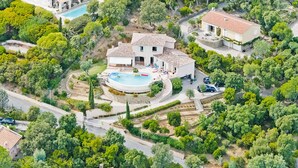 Vista aérea de una zona residencial con una casa grande que tiene piscina, rodeada de abundante vegetación y otras viviendas.
