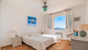 Un dormitorio con cama, mesita de noche, cómoda, ventana con vistas y ventilador de techo.