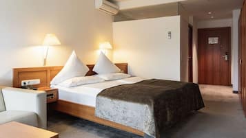 Een hotelkamer met een bed, nachtlampjes, een nachtkastje, een bureau en een deur.