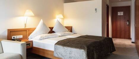 A hotel room with a bed, bedside lamps, a nightstand, a desk, and a door.