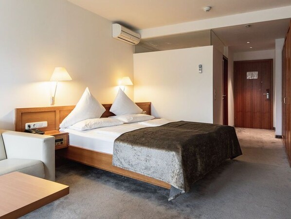 A hotel room with a bed, bedside lamps, a nightstand, a desk, and a door.
