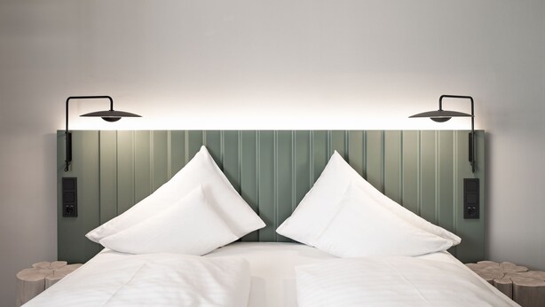 Una cama con sábanas blancas, dos lámparas de noche y un cabecero verde.