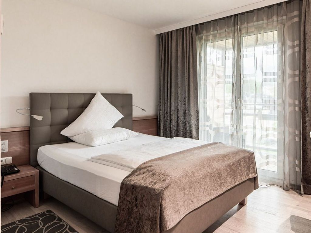 Ein modernes Hotelzimmer mit einem großen Bett, einem Nachttisch, einer Lampe und einem fenster mit Vorhängen.