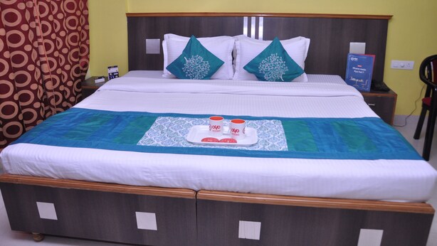 A neatly made bed with a tray of two cups and a book, a wooden headboard, and a patterned curtain. - Hotel Ashoka Residency (Patna)
