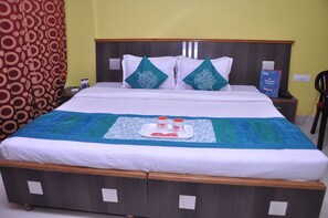 A neatly made bed with a tray of two cups and a book, a wooden headboard, and a patterned curtain. - Hotel Ashoka Residency (Patna)