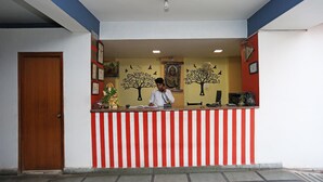 A reception desk with a red and white striped barrier, a wooden door to the left, and a wall with framed pictures and a tree mural. - Hotel Ashoka Residency (Patna)
