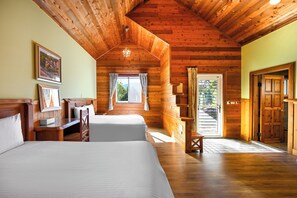 A log cabin bedroom with two beds, wooden walls, a wooden ceiling, and a window with curtains.