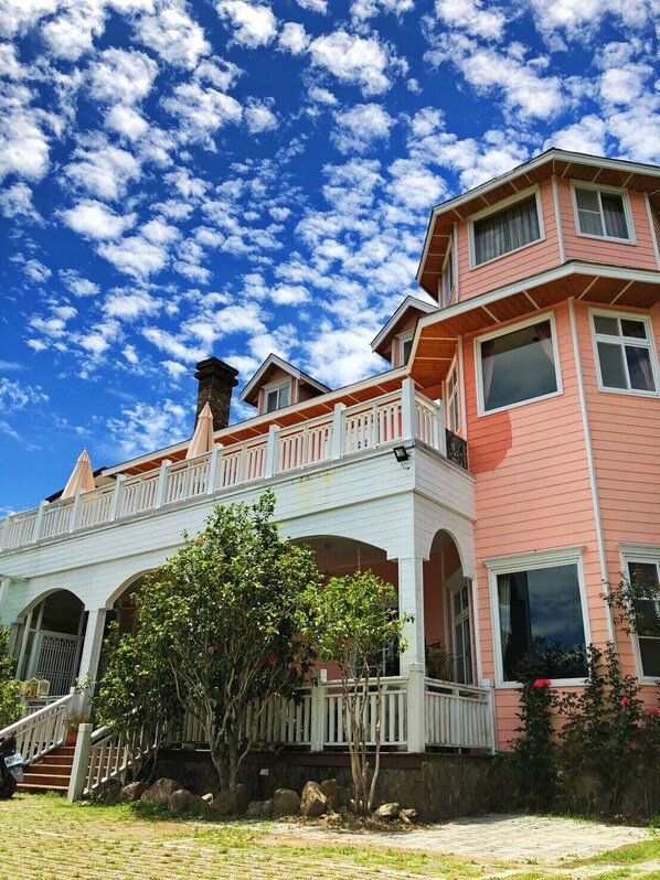 A two-story house with a balcony, a chimney, and a stone wall.