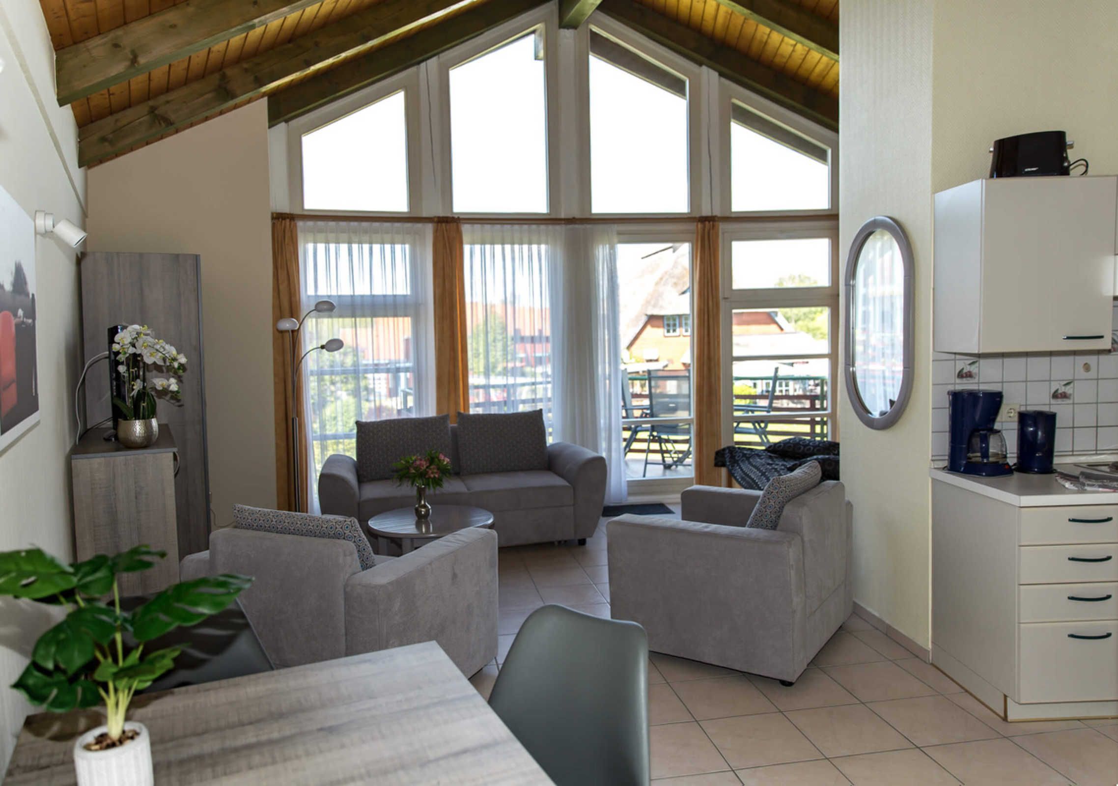 A spacious living area with a high ceiling, large windows, a kitchenette, and a dining table.