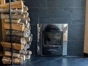 Ein moderner Kamin mit schwarzem Steinumfang, Holzstapel links und eine Metalldür.