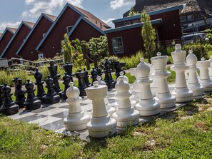 Un échiquier avec les pièces disposées à l’extérieur, entouré de verdure et avec des bâtiments en arrière-plan.