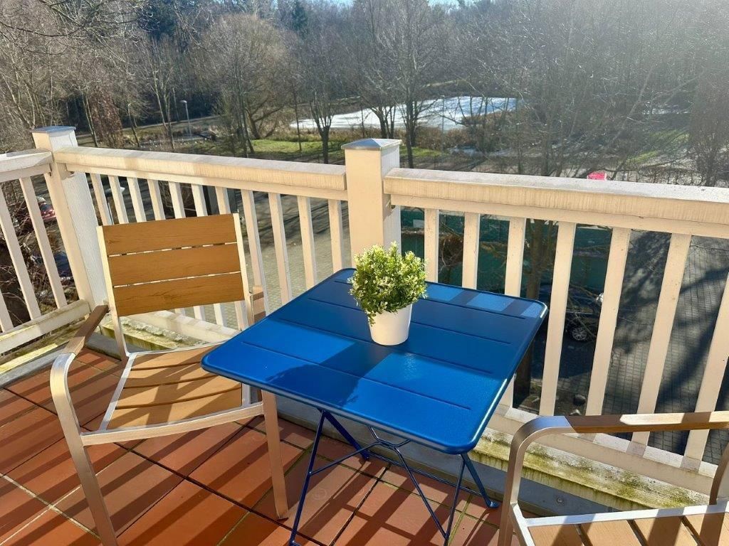 A blue metal table with a potted plant on a wooden deck with white railings.