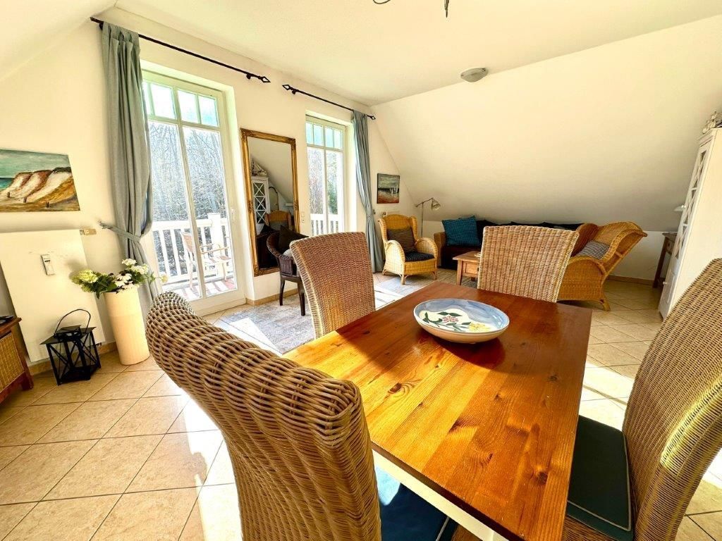 A dining area with a wooden table and wicker chairs, a balcony with a view, and a cozy seating area with cushions.