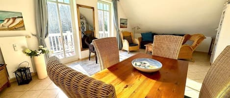 A dining area with a wooden table and wicker chairs, a balcony with a view, and a cozy seating area with cushions.