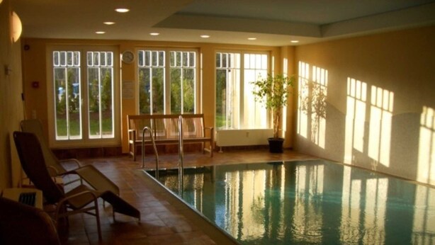An indoor swimming pool with clear glass walls, wooden deck chairs, and a potted plant. - (177) 2-room apartment Ostseeallee - apartment house dune castle (Kühlungsborn)