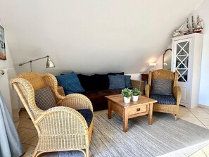 A cozy living room with wicker furniture, a dark sofa, a wooden coffee table, and a decorative cabinet. - (177) 2-room apartment Ostseeallee - apartment house dune castle (Kühlungsborn)