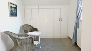 A room with a high ceiling, a white wardrobe, two wicker chairs, a small round table, and a painting on the wall. - (177) 2-room apartment Ostseeallee - apartment house dune castle (Kühlungsborn)