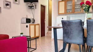 Un espacio habitable compacto con kitchenette, una zona de comedor con dos sillas, un sofá rojo y un televisor fijado a la pared.
