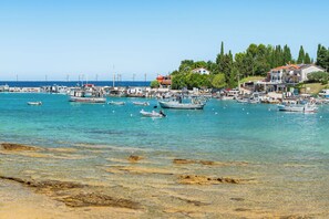 A coastal marina with boats docked, clear turquoise water, and buildings with red roofs.