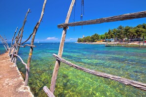 A wooden pier extending into clear blue water with a beach and trees in the background.