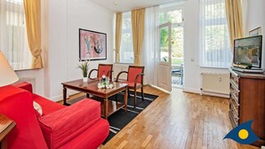 Ein gut beleuchtetes Wohnzimmer mit einem roten Sofa, einem Holzespeisesaal mit Stühlen, einem Fernseher auf einem Holzschrank und einem Gemälde an der Wand.