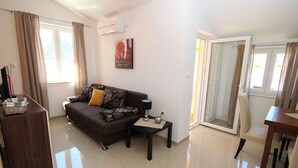 A modern living room with a sofa, a small table, a lamp, and a sliding glass door leading to an outdoor area. - Holiday apartment with shared-use pool (Baška)